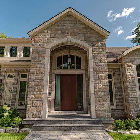 Stone house entrance with large arched doorway, steps, and beige-gray masonry facade