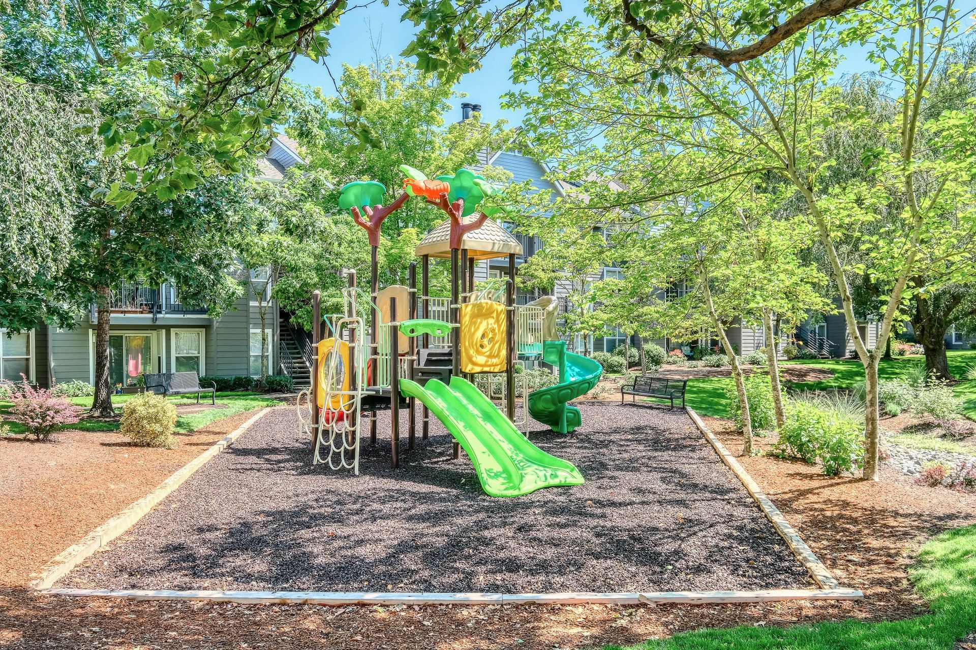 Playground with green slides and climbing structures in a shaded courtyard.