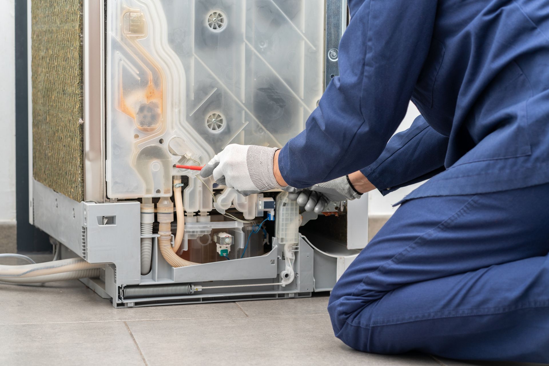 A man is kneeling on the floor fixing a dishwasher.