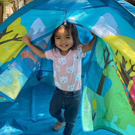 Smiling child standing inside a colorful blue play tunnel with arms raised