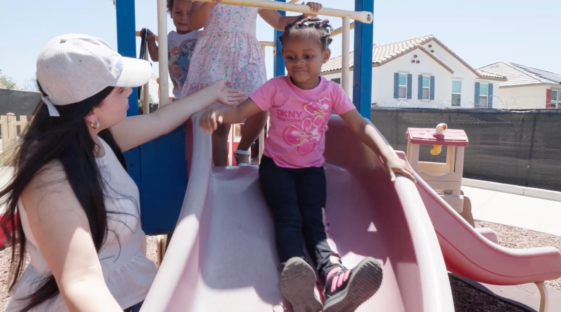 Adult helping a child on a playground slide under a sunny sky