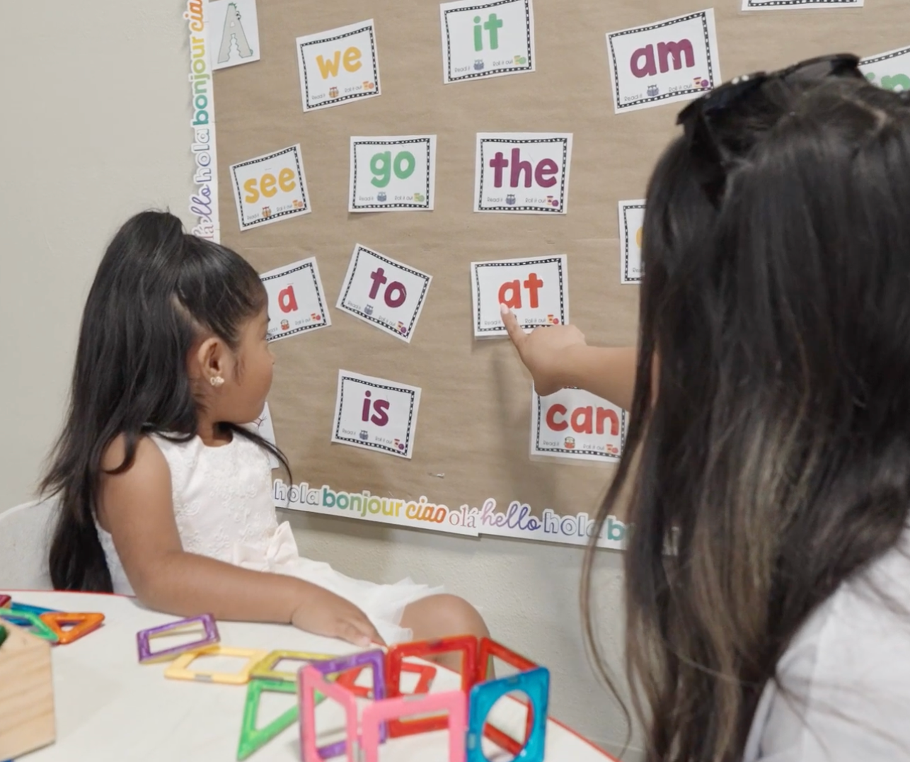 Children arranging word cards on a classroom board while seated at a table with learning materials.