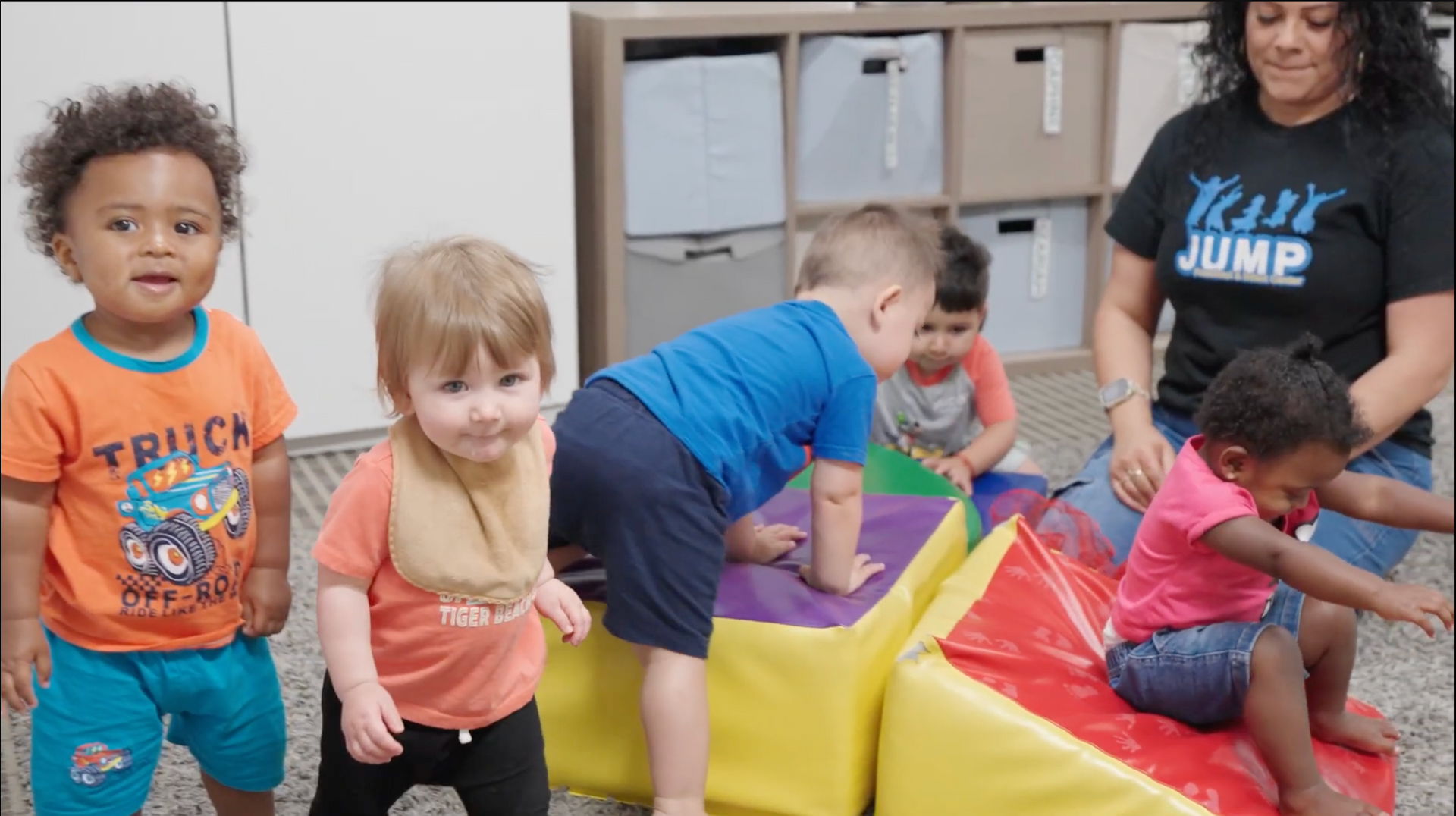 Children playing with colorful foam blocks in a classroom, guided by an adult.