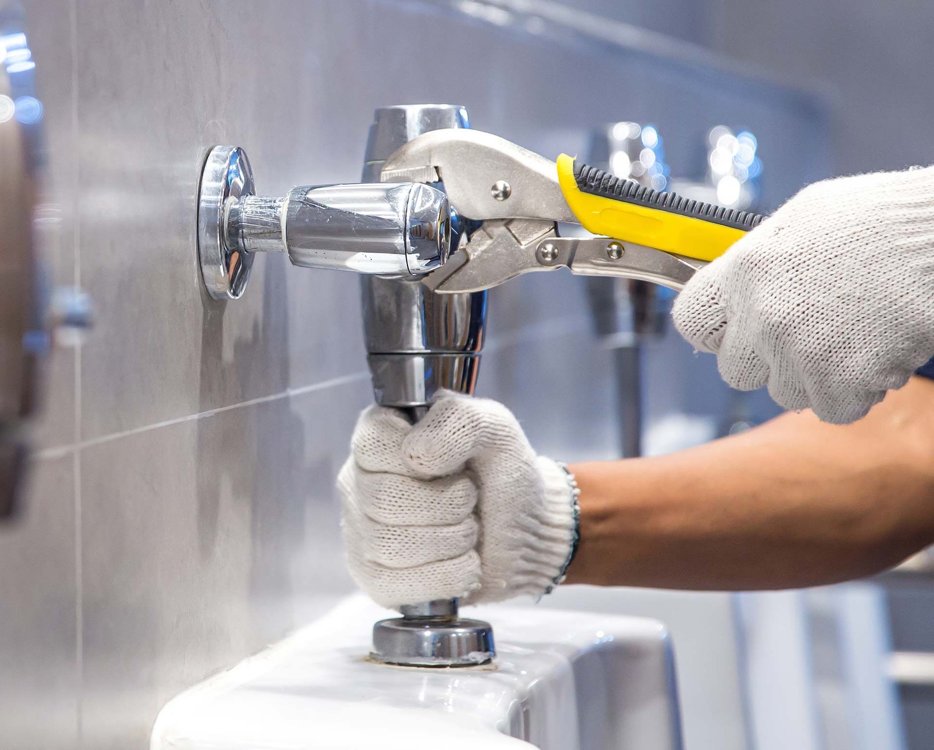 Plumber in gloves using pliers on a toilet flush valve in a public restroom in Teaneck, NJ