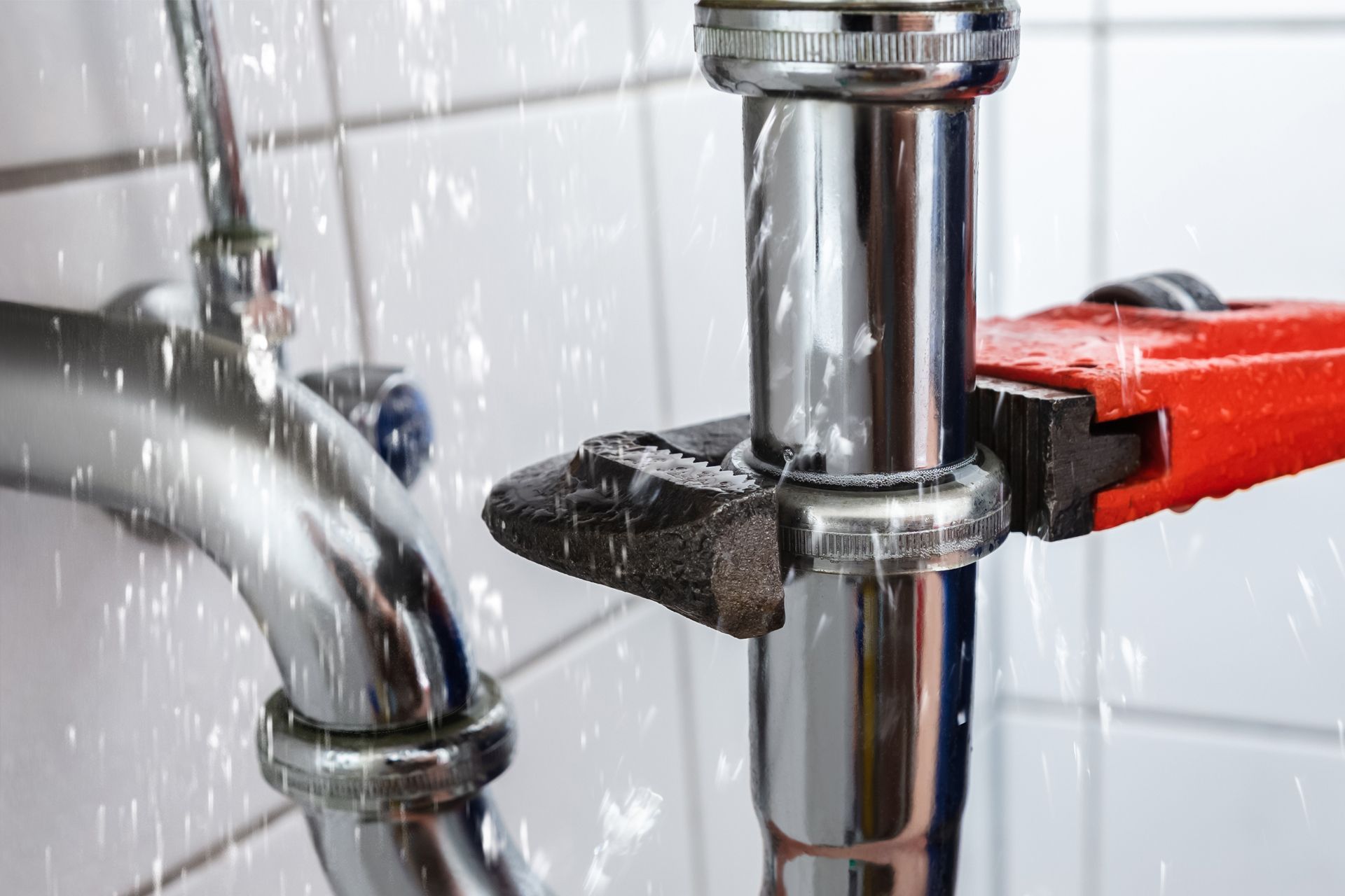 A red-handled pipe wrench grips a shiny chrome plumbing pipe against white tile in Teaneck, NJ