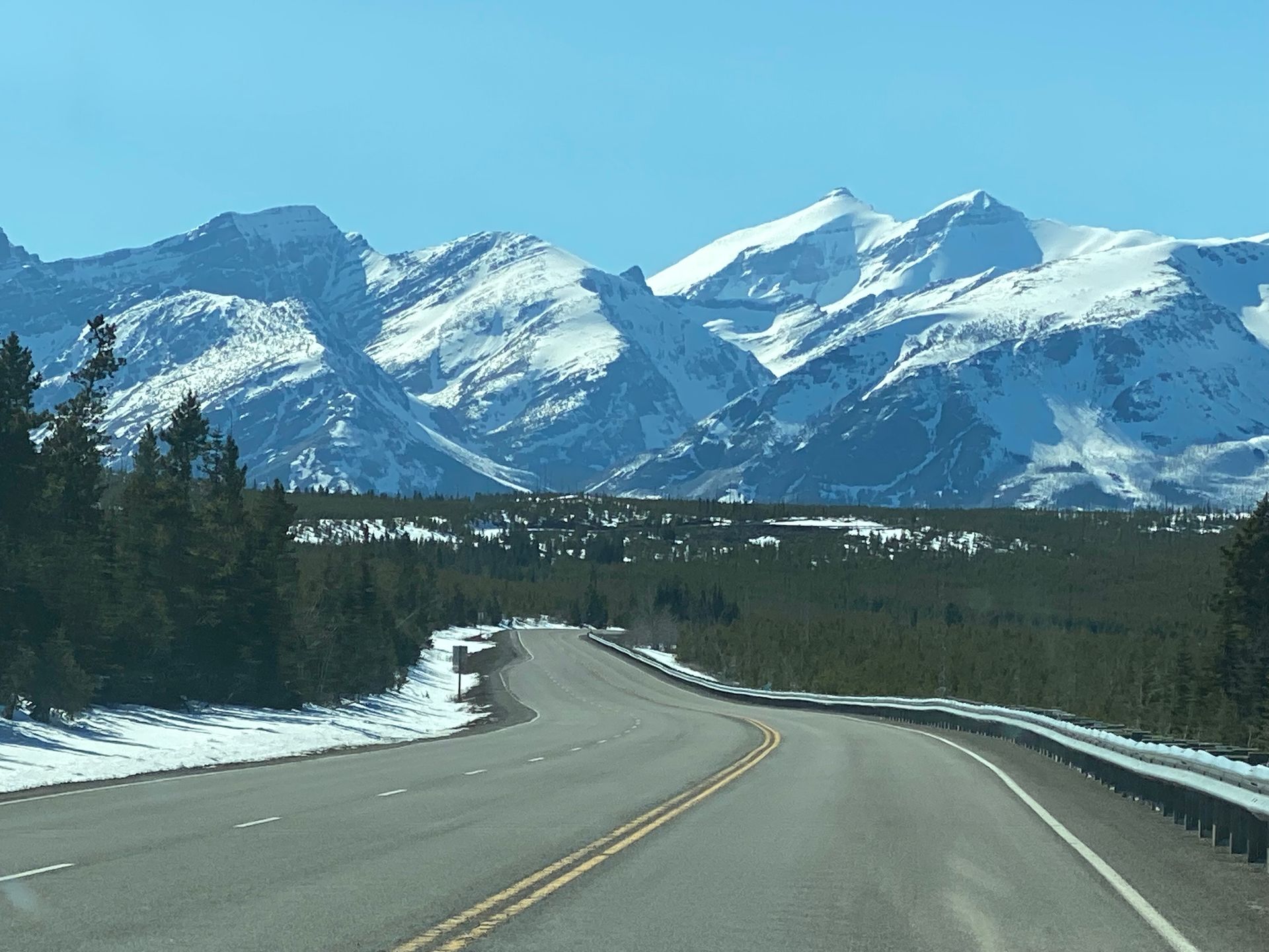 Snowy mountain range beyond a winding highway under a clear blue sky