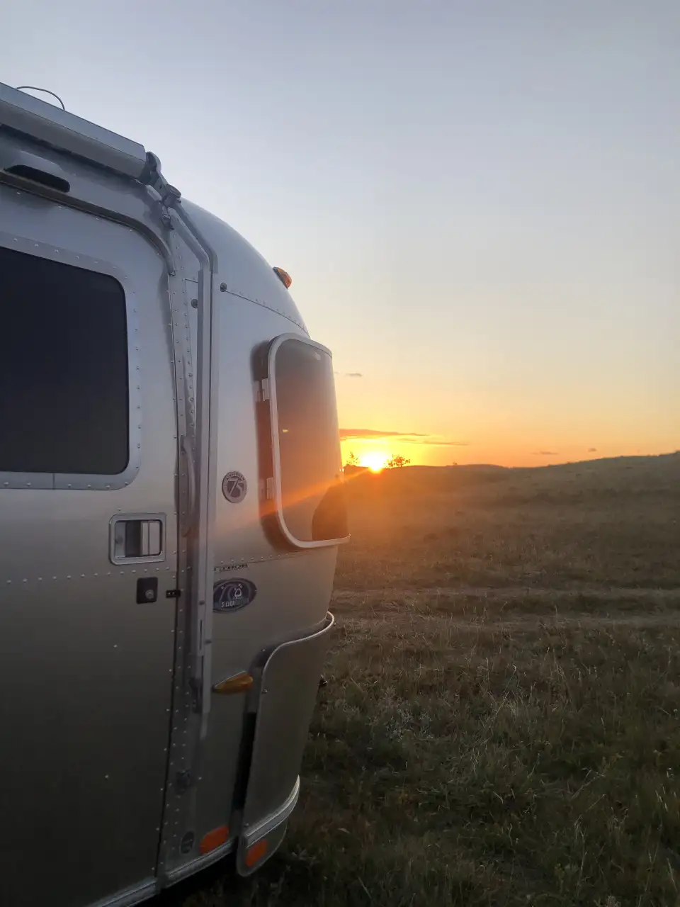 Silver trailer at sunset in an open field, with the sun low on the horizon.