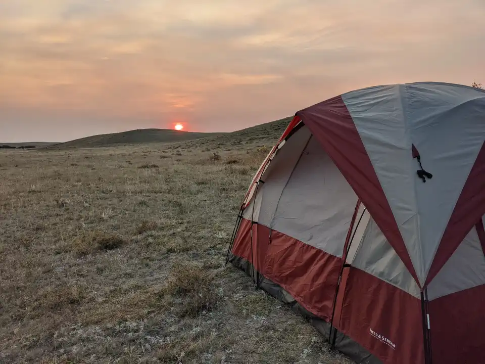 Red and gray camping tent on frosty grass at sunrise in a open field.
