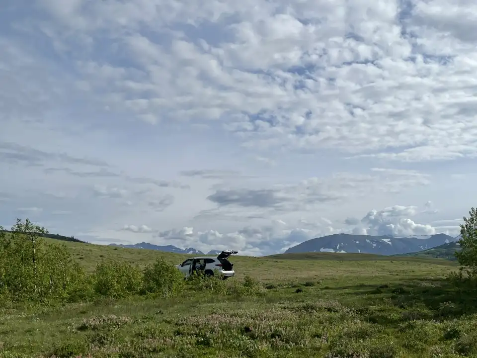 Motorcyclist on a grassy plain with mountains and cloudy sky in the background