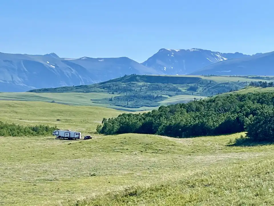 White truck in green meadow with mountains and blue sky in the background