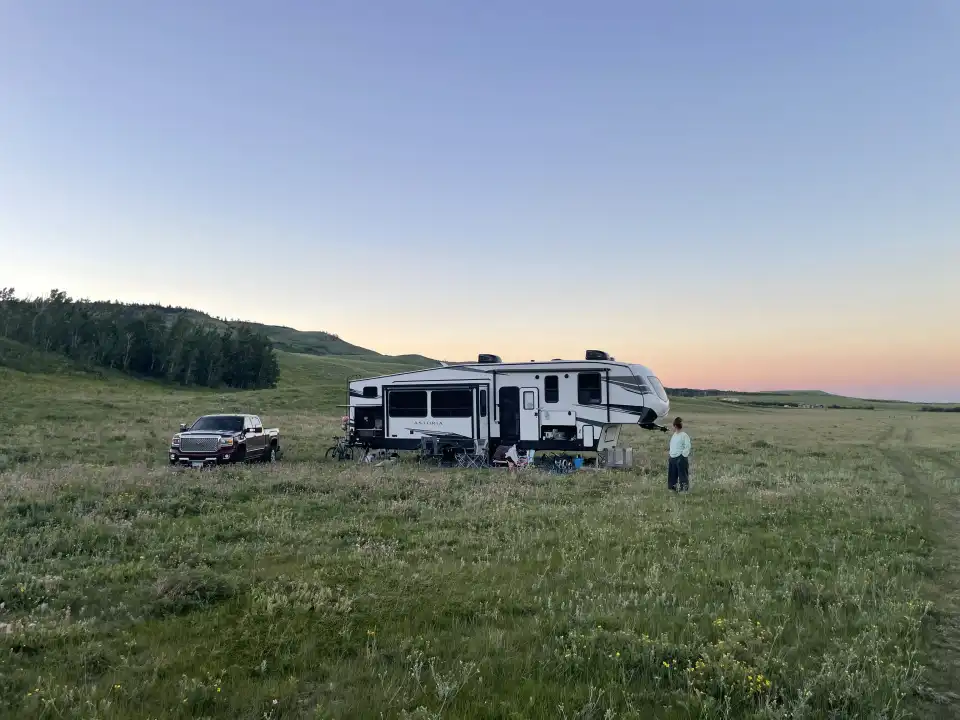 RV and SUV parked in a grassy field at sunset, with a person standing nearby.