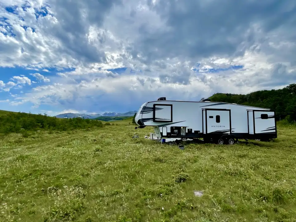 White RV trailer in a grassy field under a cloudy blue sky