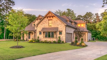 A large house with a driveway leading to it is surrounded by trees.