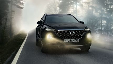 A black car is driving down a foggy road.