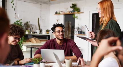 A group of people are sitting around a table with laptops.