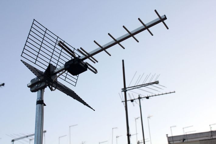 Antenne televisive sui tetti stagliano un cielo pallido, una grande antenna nera in primo piano.