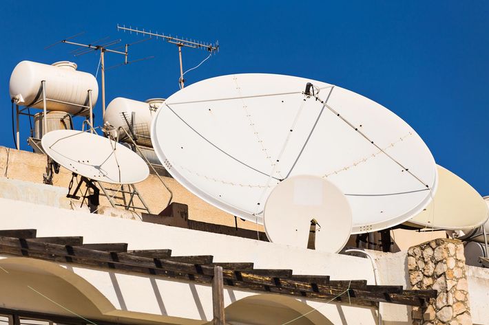 Grandi parabole satellitari bianche su un tetto, sullo sfondo di un cielo azzurro limpido.