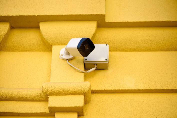 Telecamera di sicurezza bianca montata su una parete gialla, rivolta verso l'esterno.