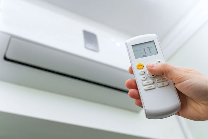 Una mano che impugna un telecomando punta verso un condizionatore d'aria a parete, che indica 17°C.