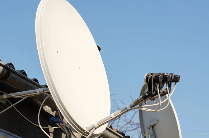 Due parabole satellitari bianche contro un cielo azzurro, con cavi e apparecchiature montate.