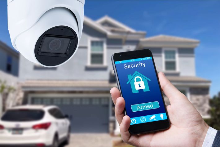 Telecamera di sicurezza e smartphone che mostrano un'app per la sicurezza domestica davanti a una casa.