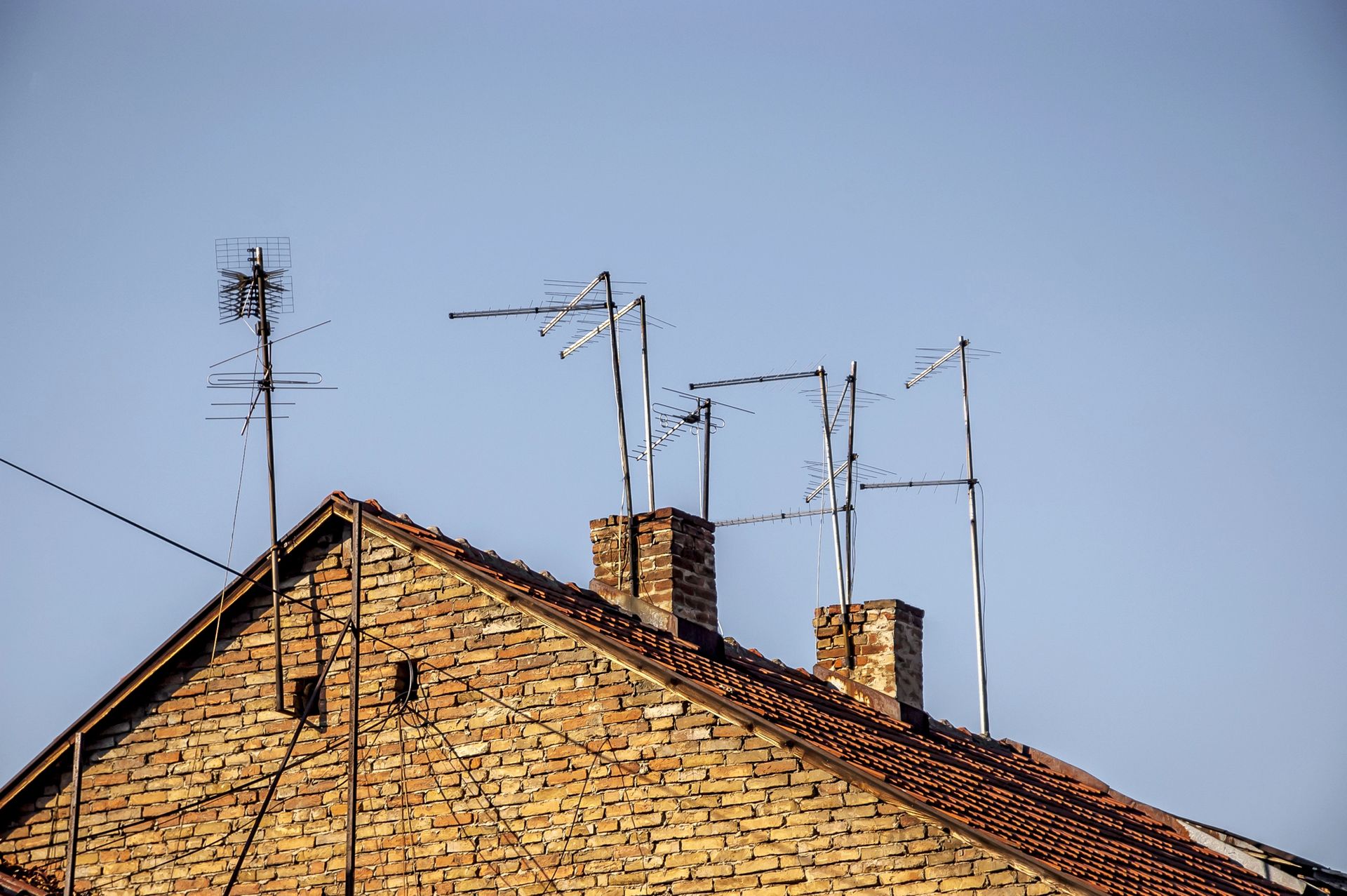 Tetto di mattoni con diverse antenne televisive sullo sfondo di un cielo azzurro.