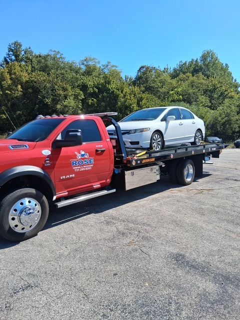 Red tow truck carrying a white sedan on a sunny day.