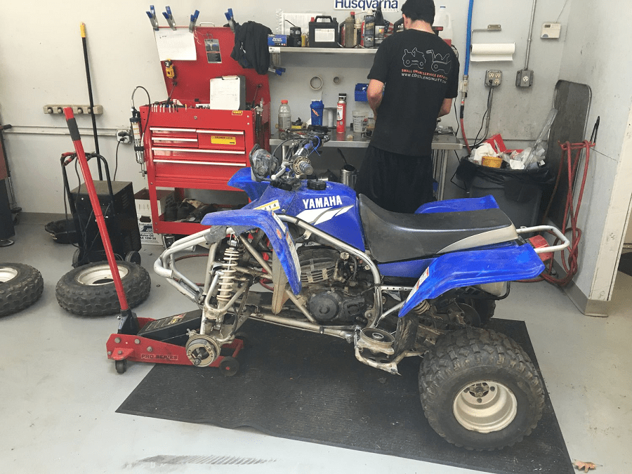 Blue Yamaha ATV being worked on in a garage; a mechanic is present.