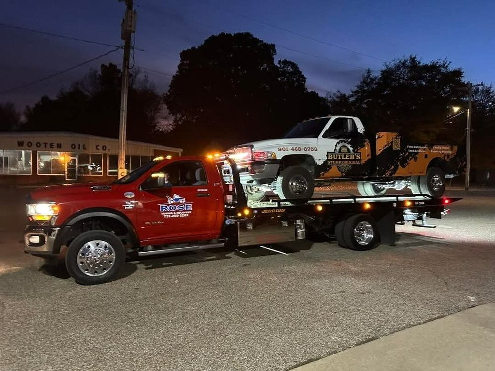 Red tow truck hauling a white pickup truck with logo, at night, street setting.