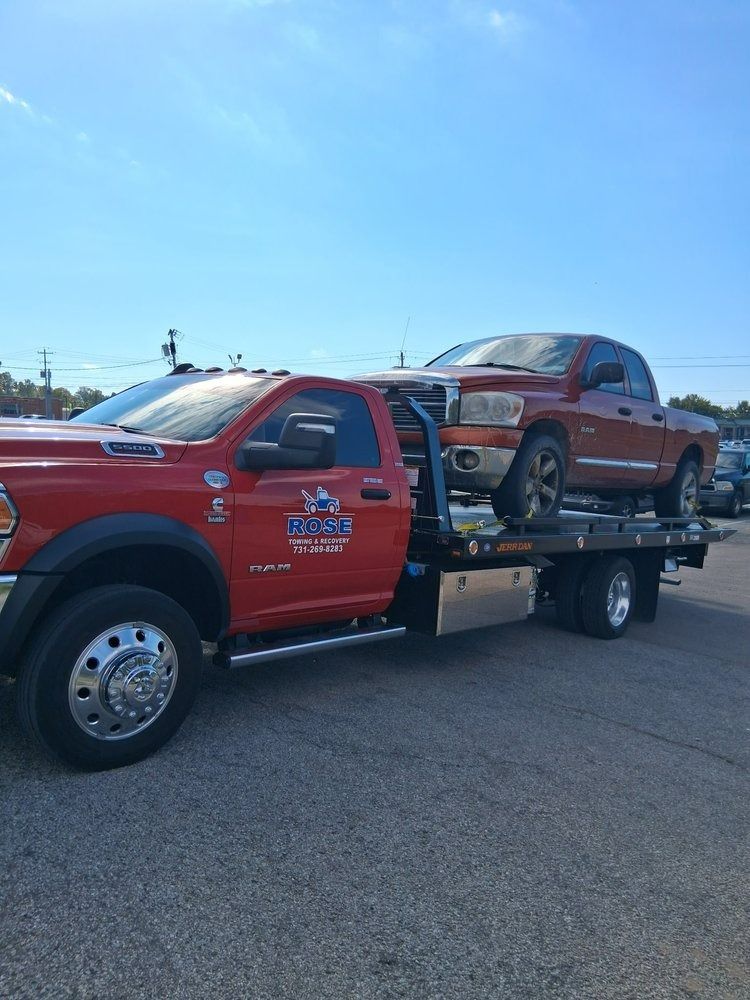 Red tow truck towing a brown pickup truck on a sunny day.