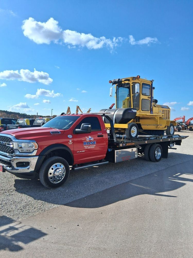 Red tow truck transporting a yellow construction machine on a sunny day.