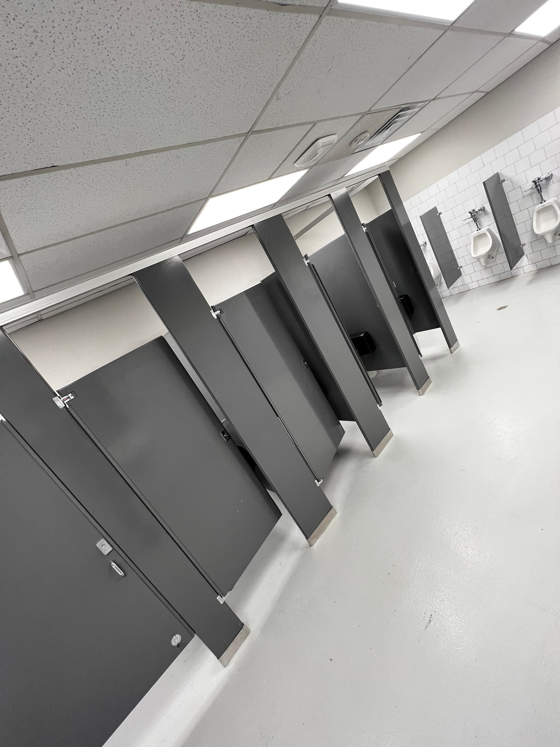 Tilted view of a public restroom with gray stalls and white tiled floor.