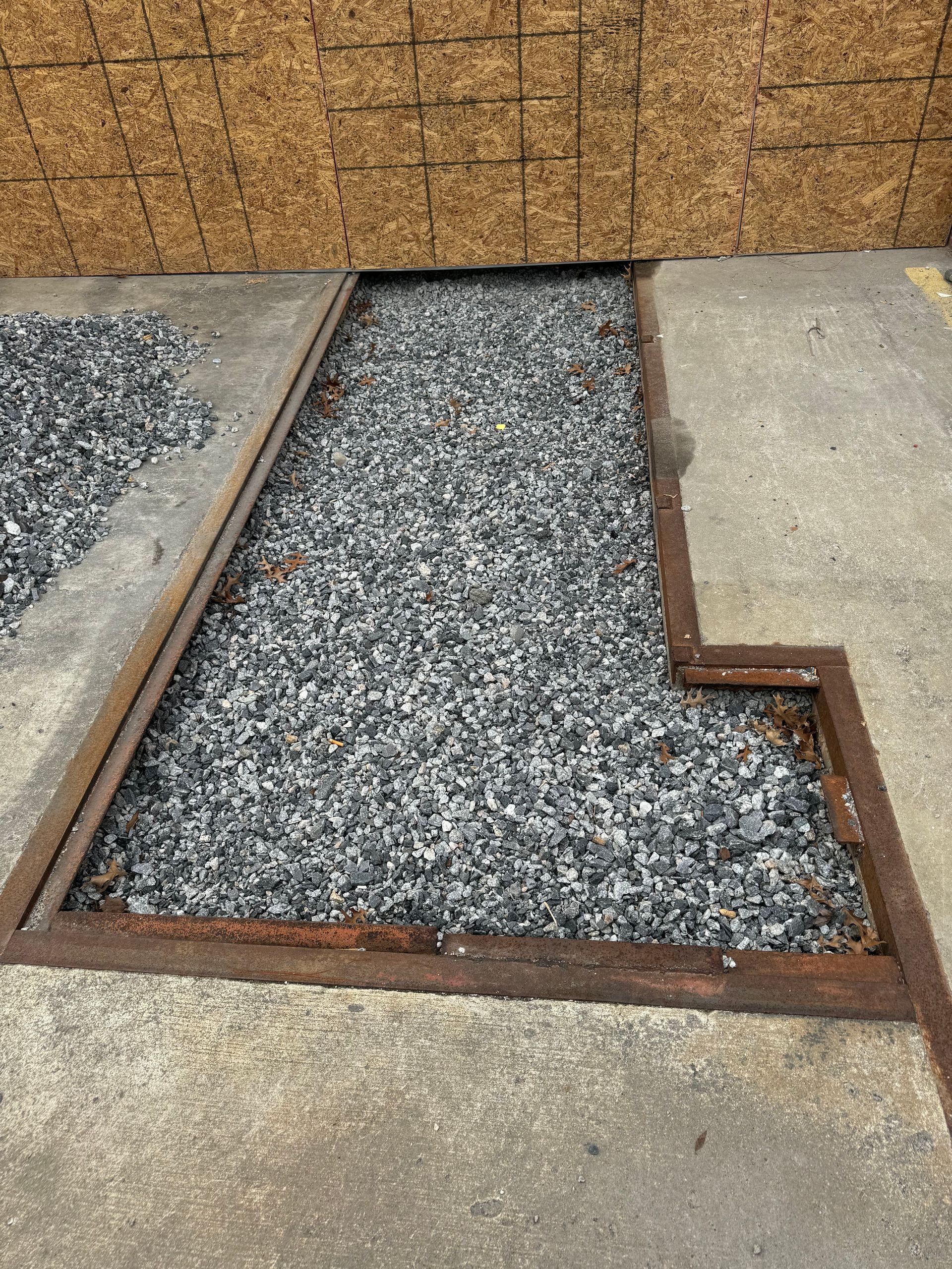 Rust-edged gravel drainage channel between concrete slabs in a yard
