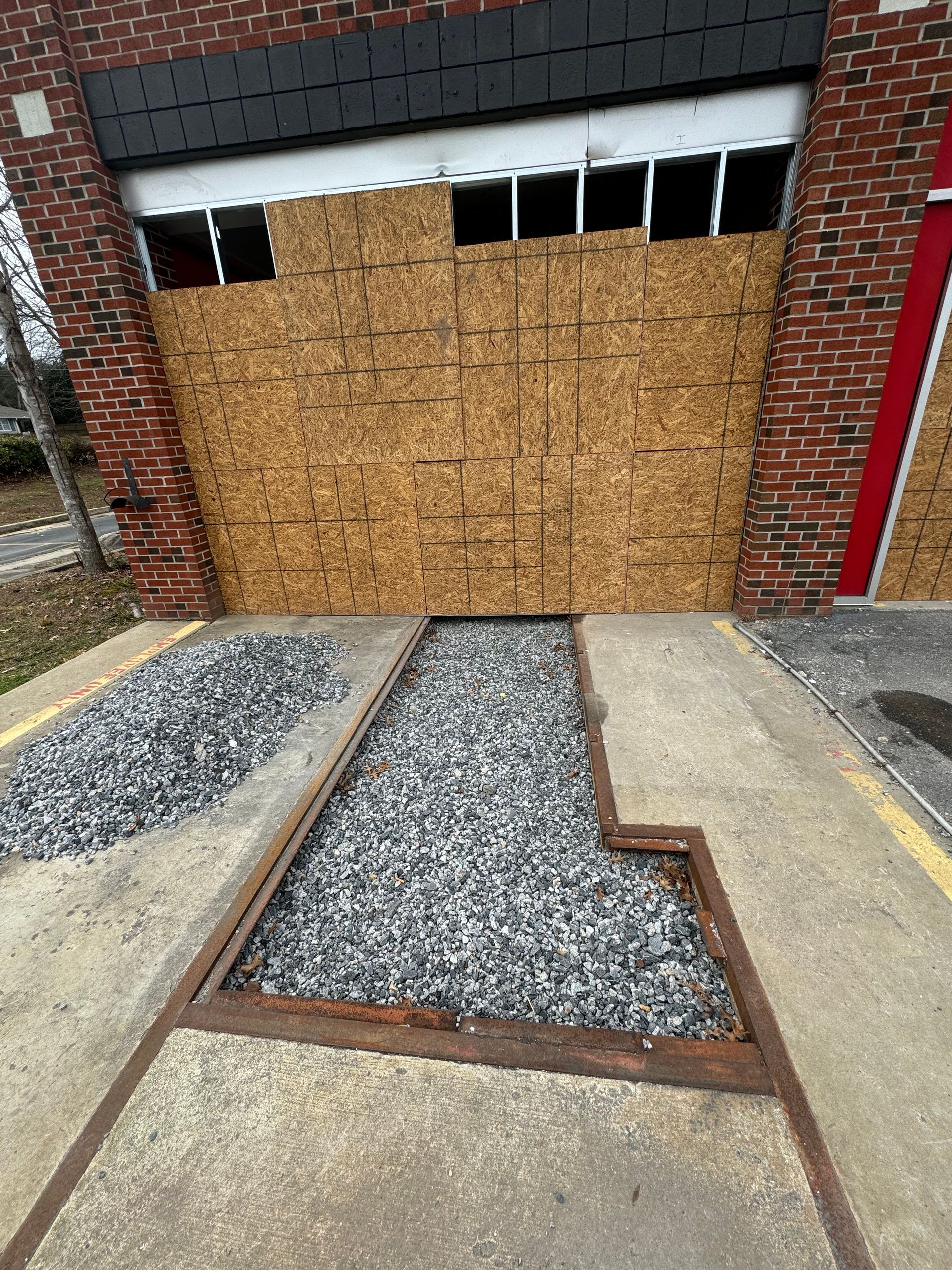 Boarded-up garage door behind a gravel walkway and brick walls