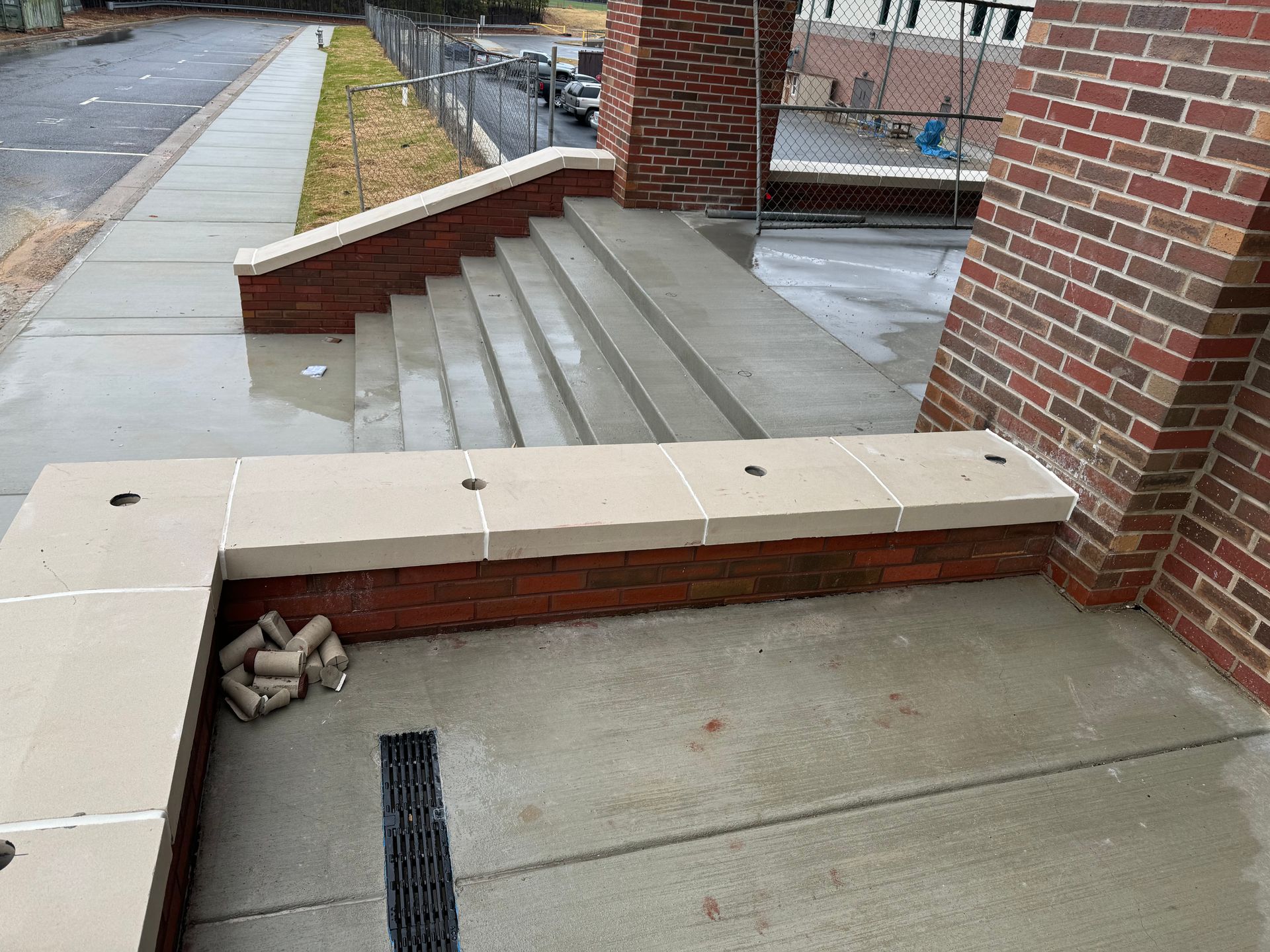 Wet concrete steps and brick ramp beside a building entrance with a black drainage grate.