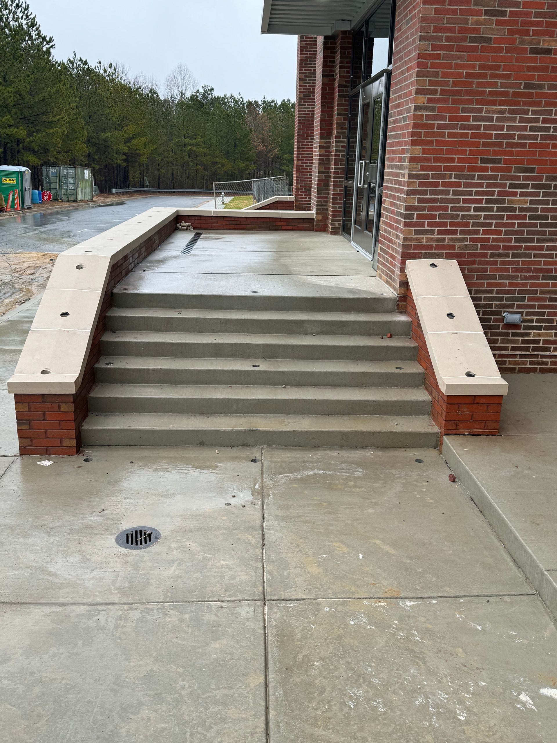 Concrete steps and ramp beside a brick building entrance on a wet sidewalk.