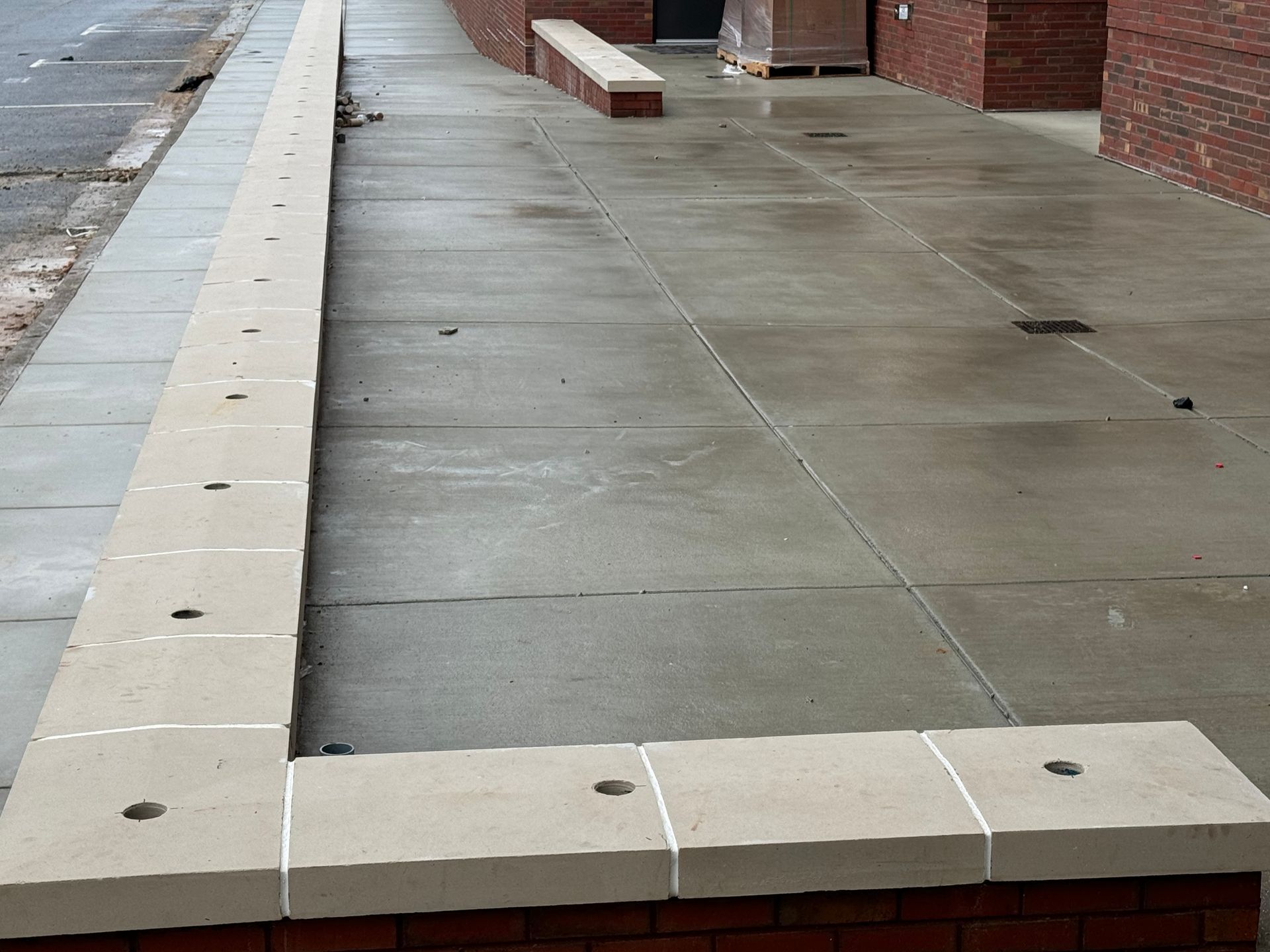 Concrete sidewalk ramp along a brick building, with wet pavement and curb stones.