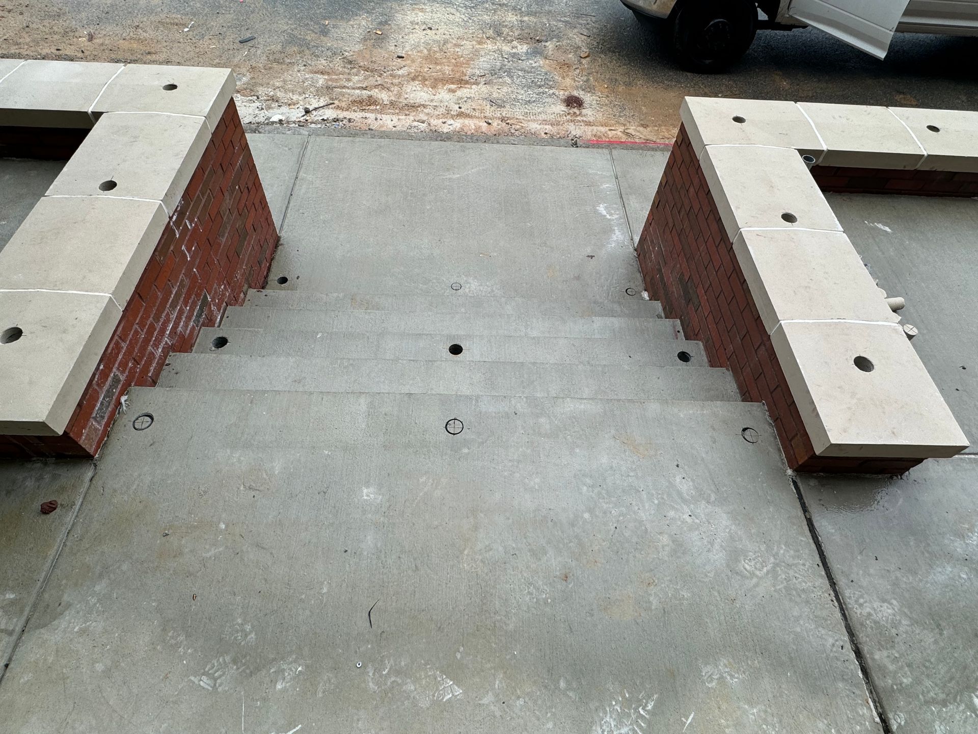 Concrete parking barrier between two brick curbs with bolt holes and a car partially visible at top right
