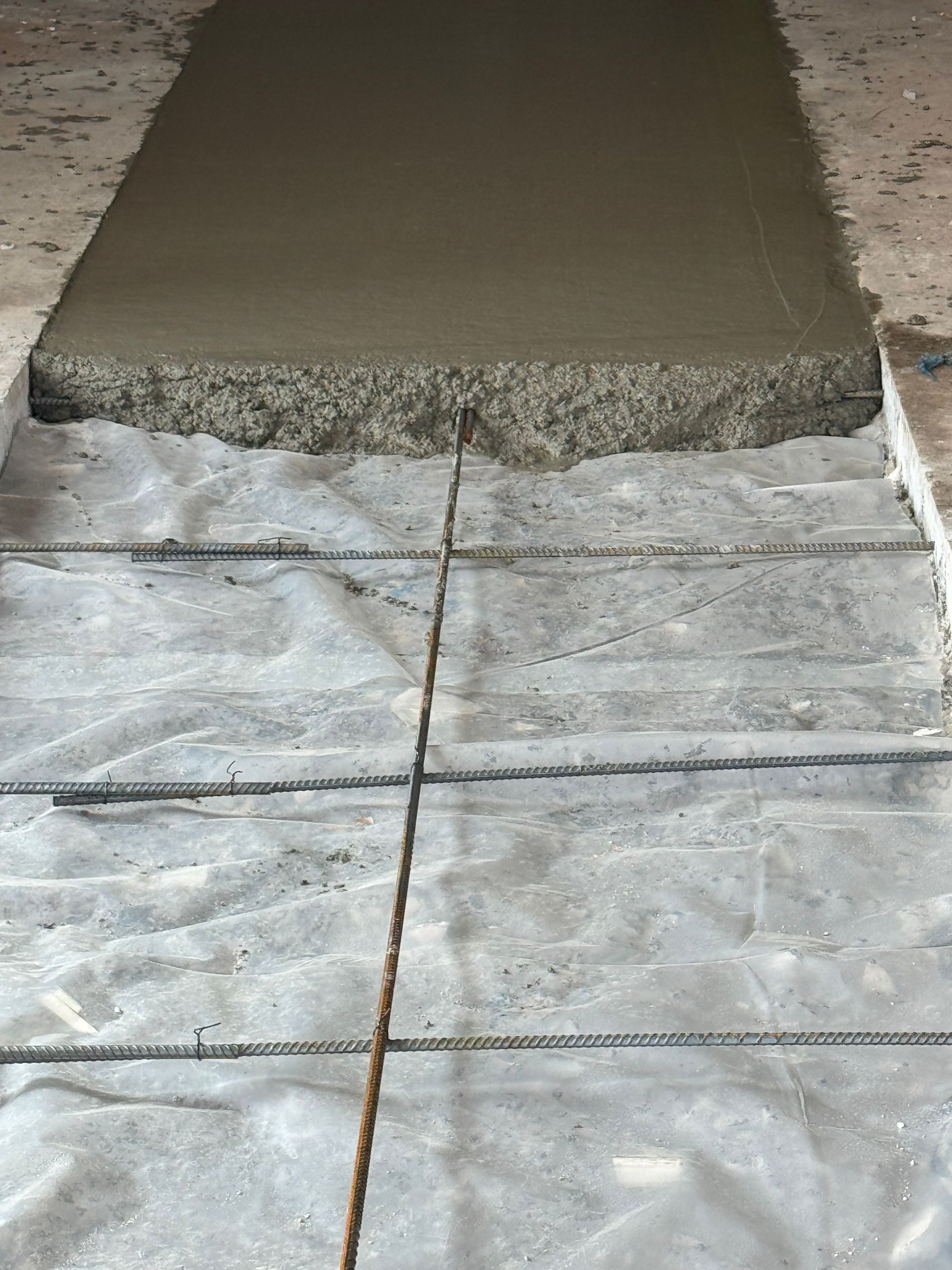 Fresh concrete slab beside a tarp-covered walkway during sidewalk repair
