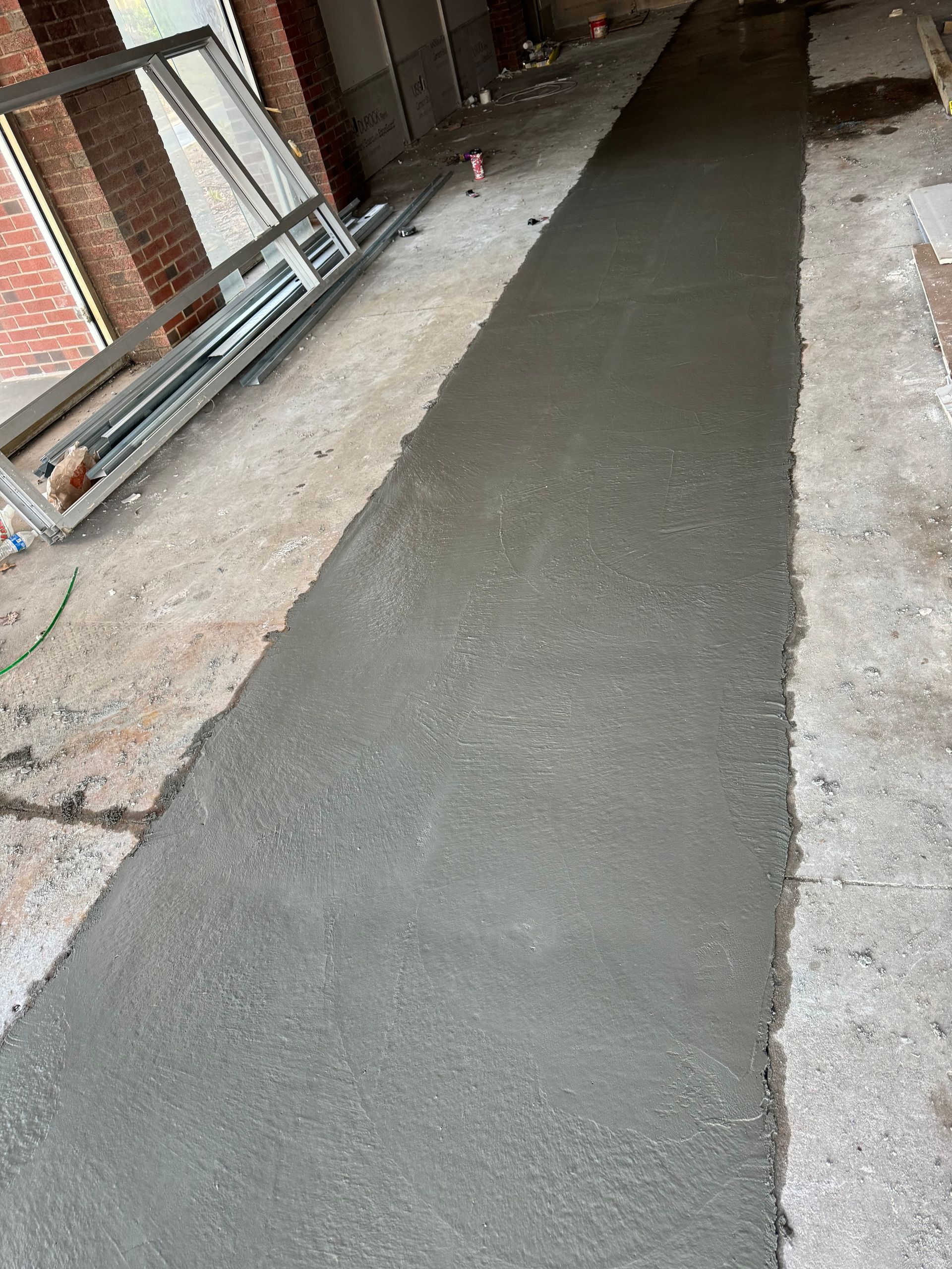Fresh concrete walkway in a narrow indoor corridor with pipes along the left wall