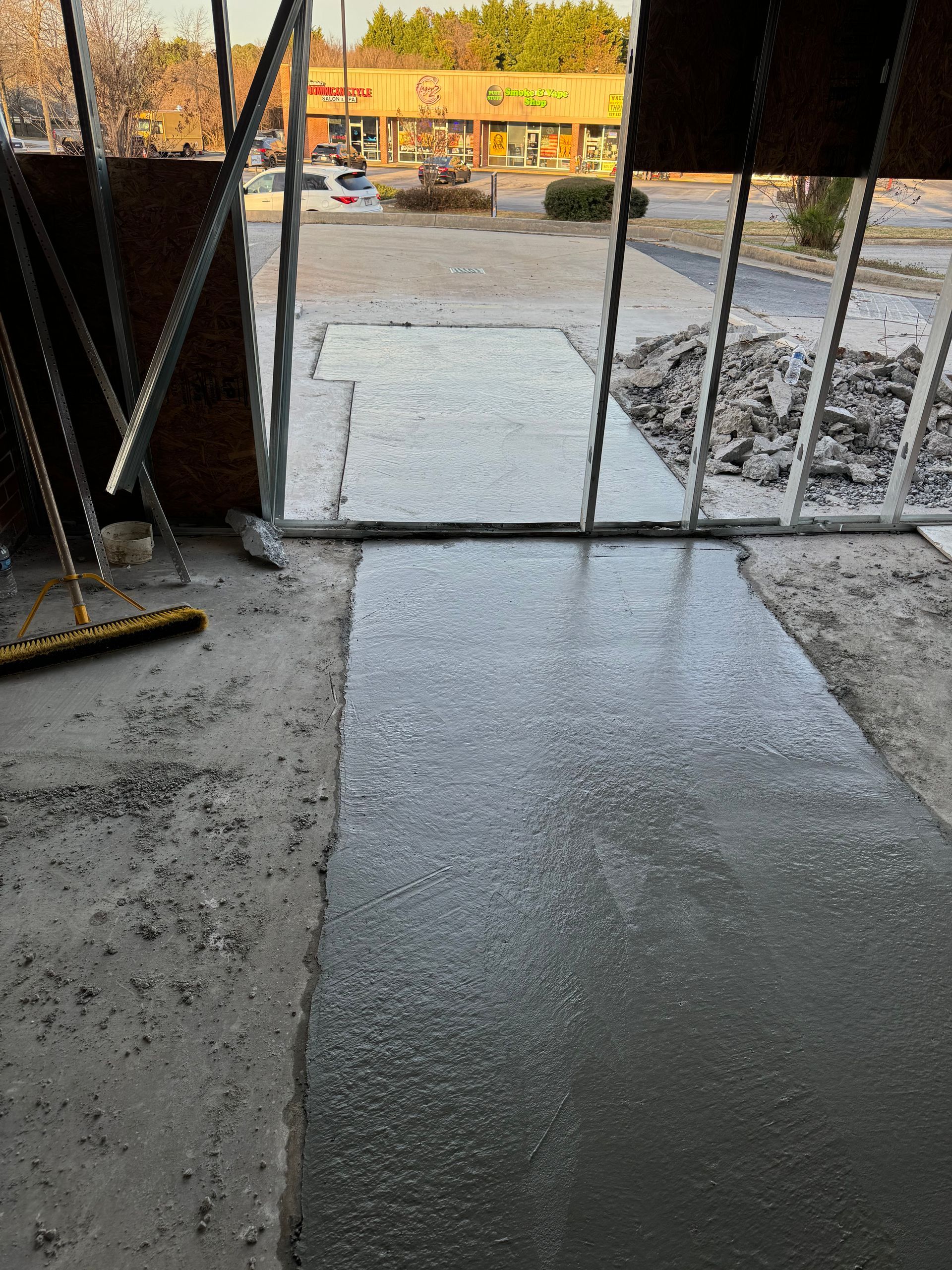 Wet concrete walkway leading to a metal gate at a construction site, with tools and rubble nearby