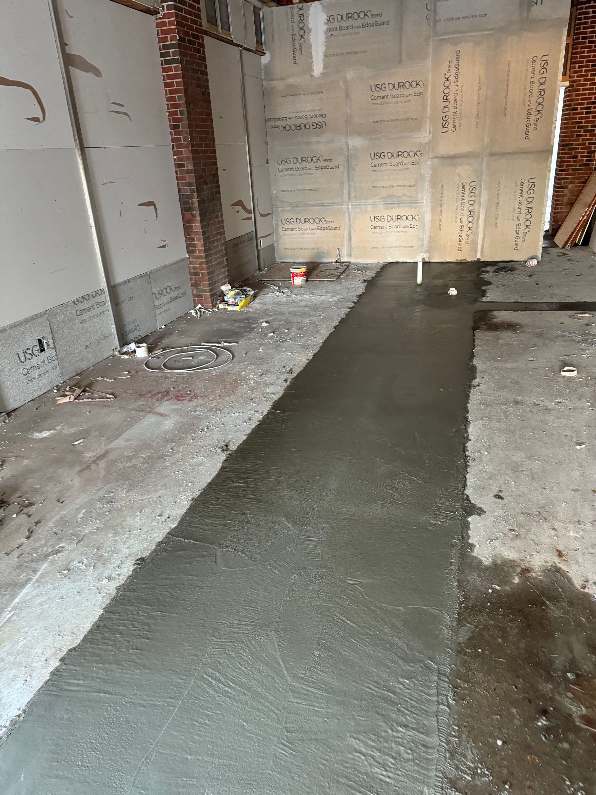 Narrow wet concrete corridor with scattered debris and a boarded doorway at the end