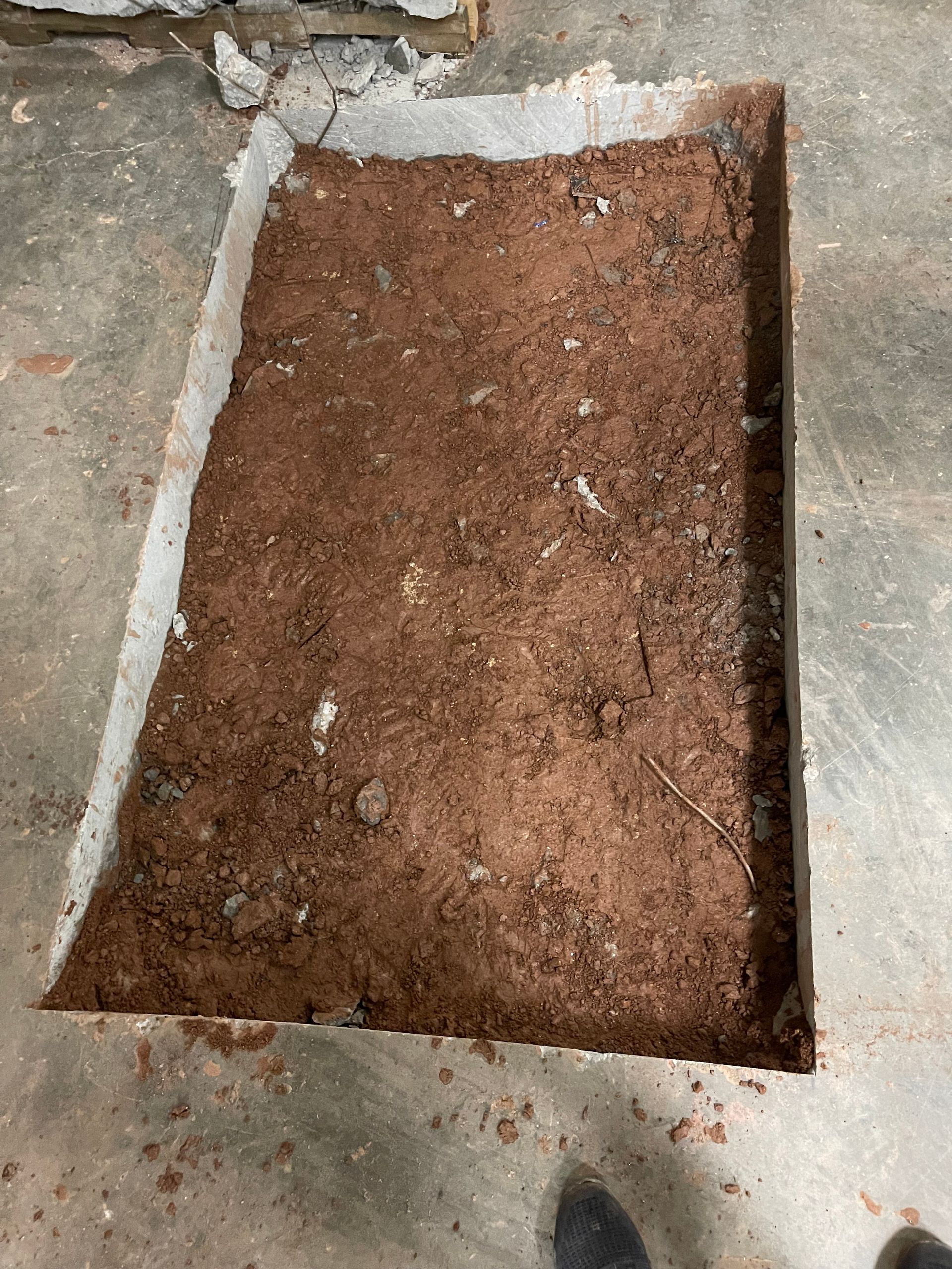 Rectangular cutout in a concrete floor filled with brown soil or dirt