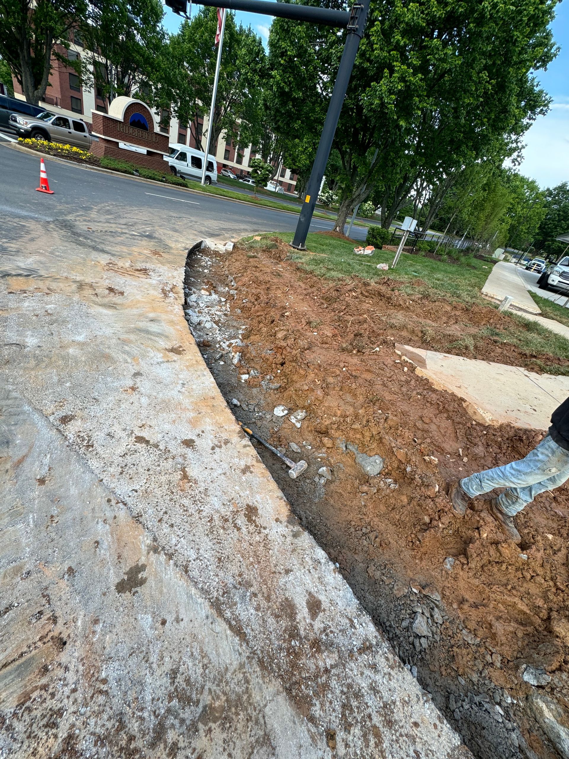 Roadwork trench beside a tree-lined sidewalk, with exposed dirt and gravel along the curb.