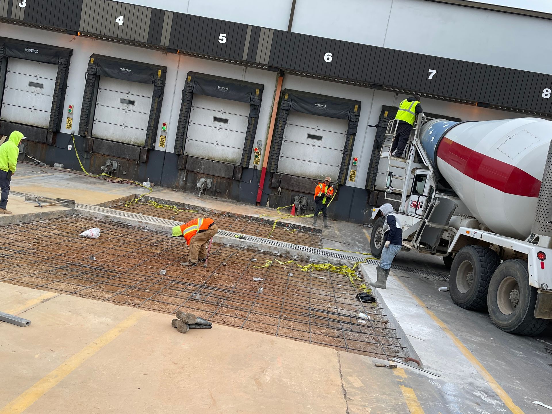 Workers repairing concrete at a warehouse loading dock beside a cement mixer truck