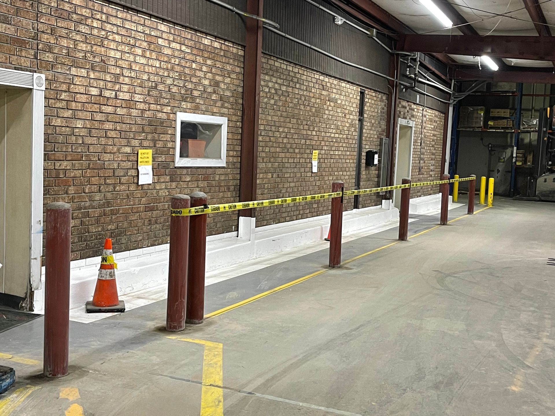 Brick-walled loading dock with yellow barriers, white curb blocks, and orange traffic cones