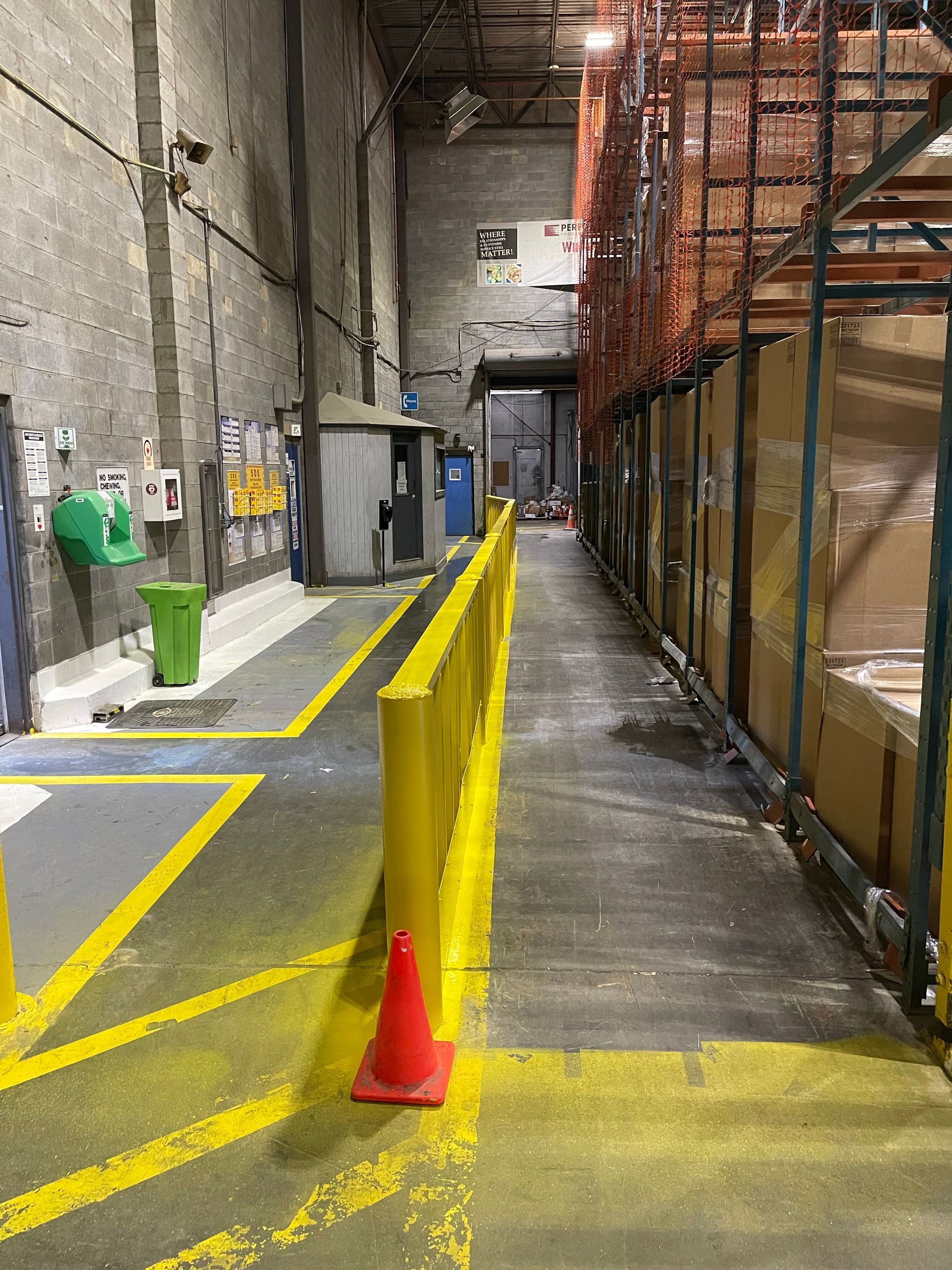 Industrial corridor with yellow safety barrier, orange cone, and scaffolding along a narrow walkway