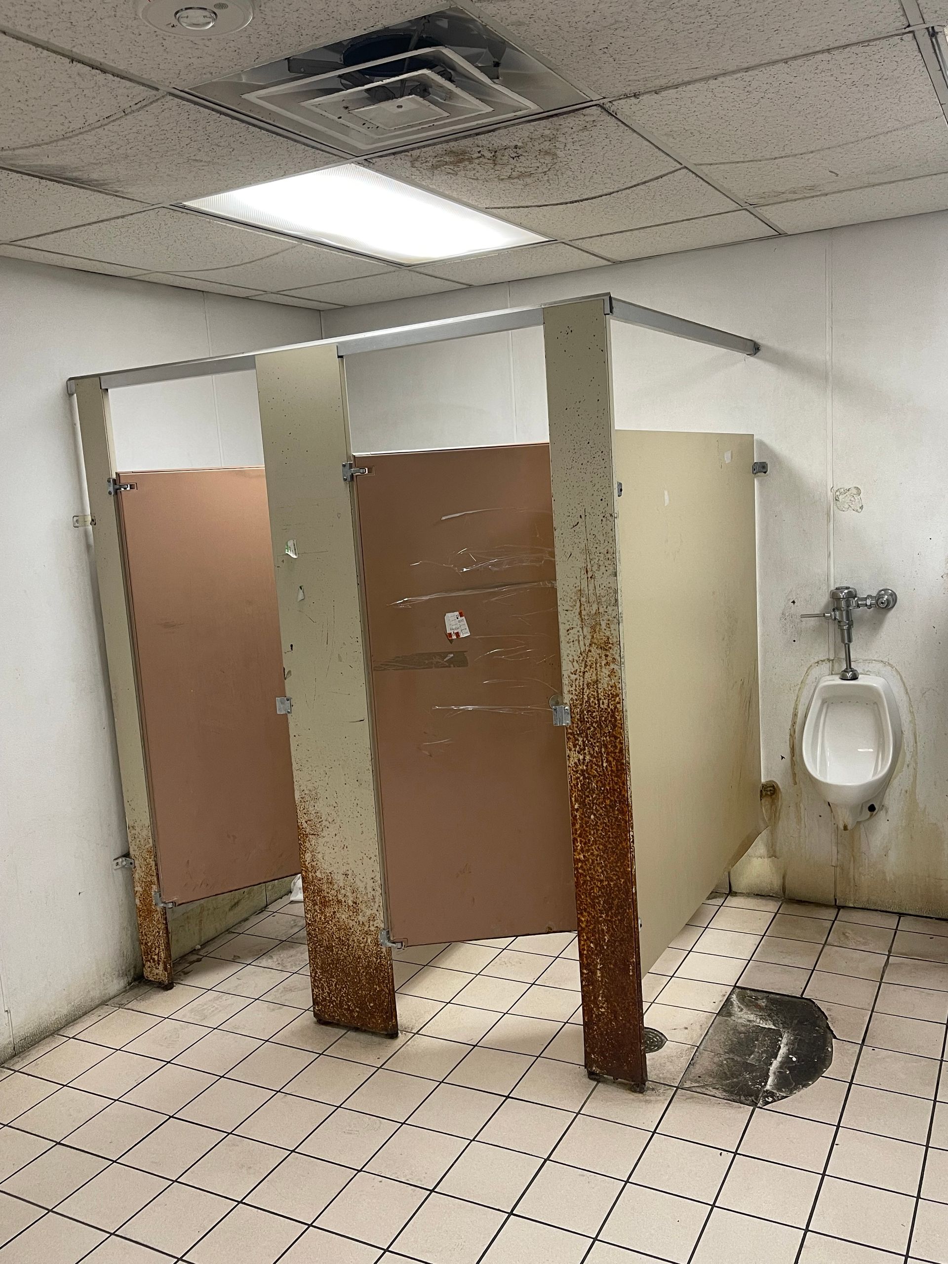 Public restroom with three stall doors, a toilet, and an exposed ceiling tile leak stain