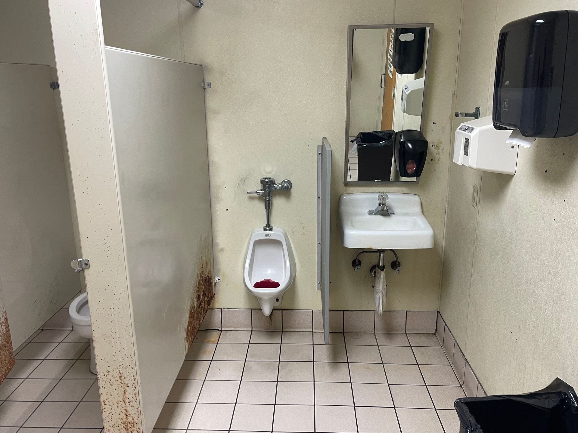 Public restroom with a urinal, sink, stalls, and tiled floor in a narrow beige room