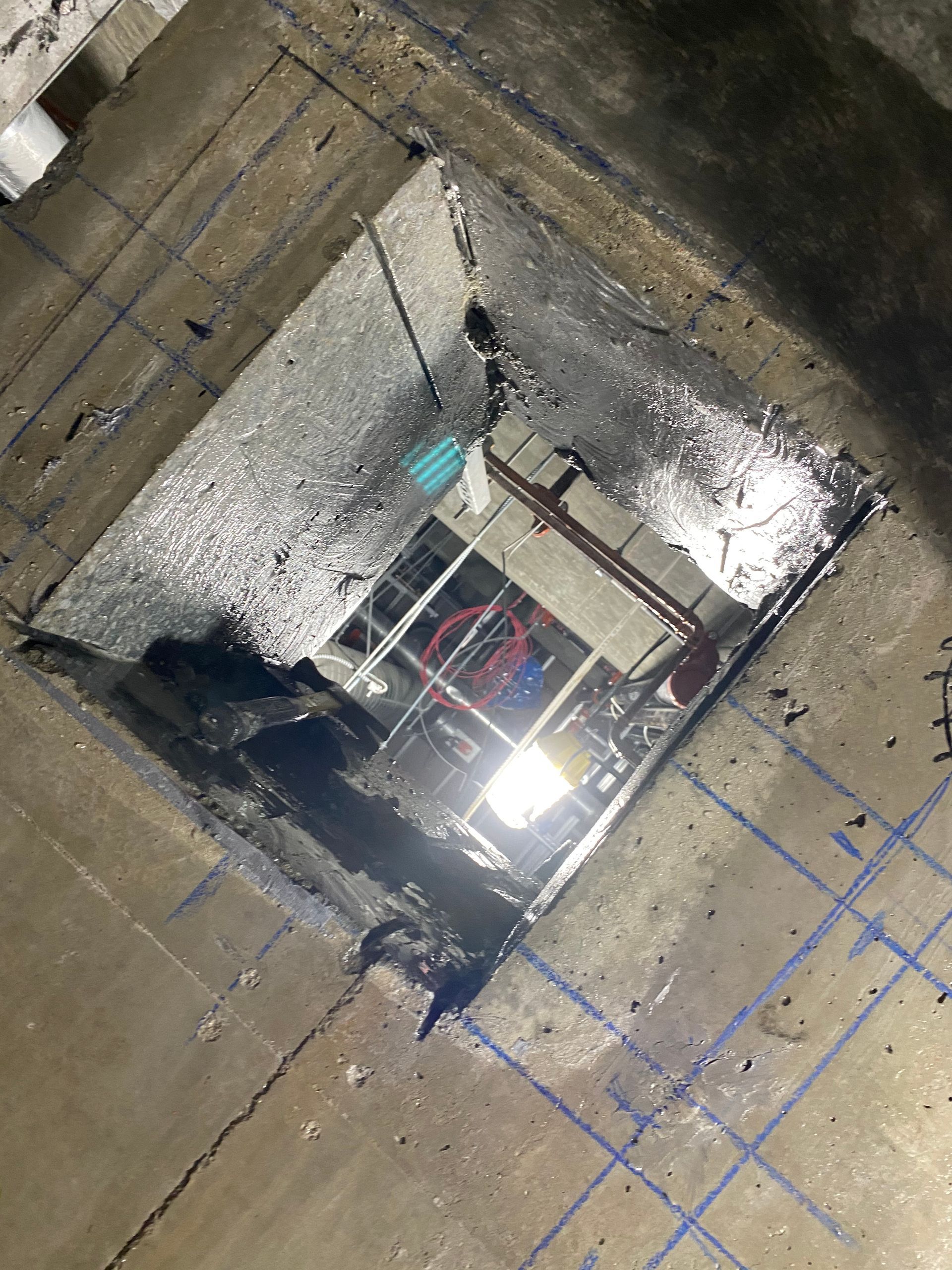 Tilted view of a building shaft with a metal ladder, bright light, and wet concrete walls.